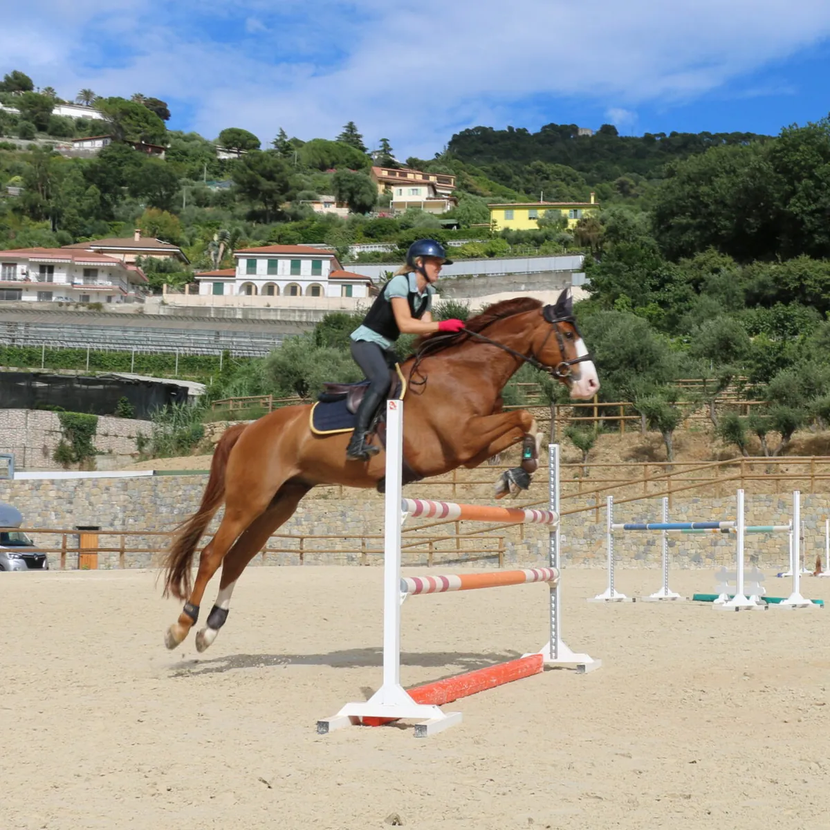 Cavalière en plein saut d’obstacle au centre équestre Liguria Jumping, collines de la riviera ligure en arrière-plan